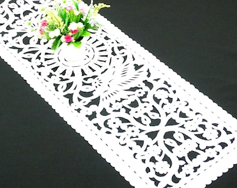 May include: White lace table runner with a delicate floral pattern. The runner is made of a lightweight material and has a scalloped edge.