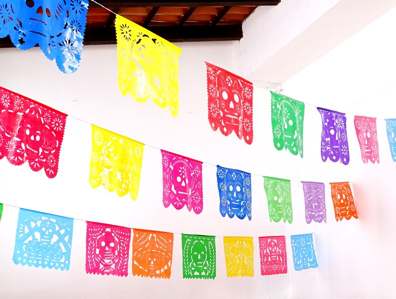 May include: A colorful string of paper banners with a skull design, perfect for a Day of the Dead celebration. The banners are in various colors, including red, yellow, blue, green, purple, and orange.