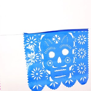 May include: A colorful paper banner with three flags. The middle flag is blue with a white skull and crossbones design. The flag on the left is pink and the flag on the right is green.