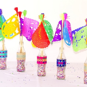 May include: Five glass bottles filled with colourful confetti and topped with colourful paper cutouts, resembling flags, with tassels. The bottles are decorated with colourful patterned bands.