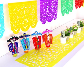 May include: A festive display featuring colorful Mexican-themed decorations. The scene includes paper banners in various colors, miniature figures in traditional attire, and potted plants. A yellow paper runner with cut-out designs adds to the celebratory atmosphere.