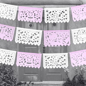 May include: A string of pink and white paper banners with cut-out designs. The banners feature baby-related themes, such as prams, stars, and hearts.