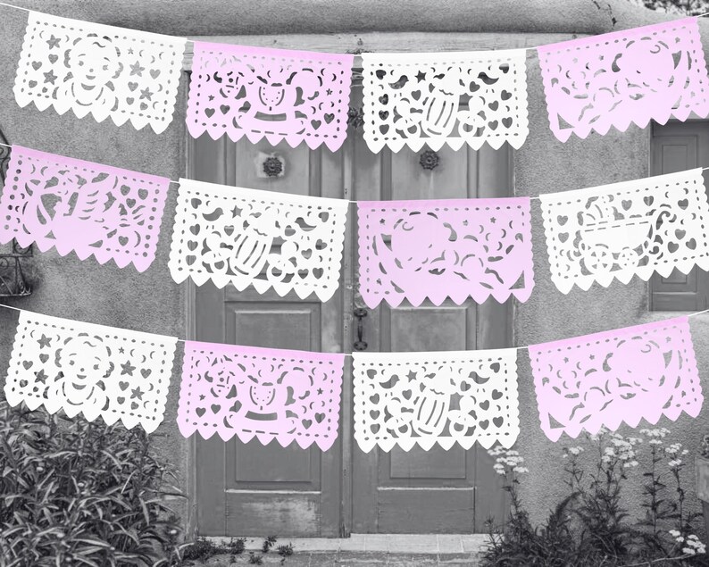 May include: A string of pink and white paper banners with cut-out designs. The banners feature baby-related themes, such as prams, stars, and hearts.