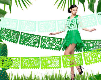 May include: A woman in a green dress dances in front of a green and white paper garland. The garland is made of cut-out paper shapes, including flowers, birds, and musical instruments. The garland is hanging from a white background.