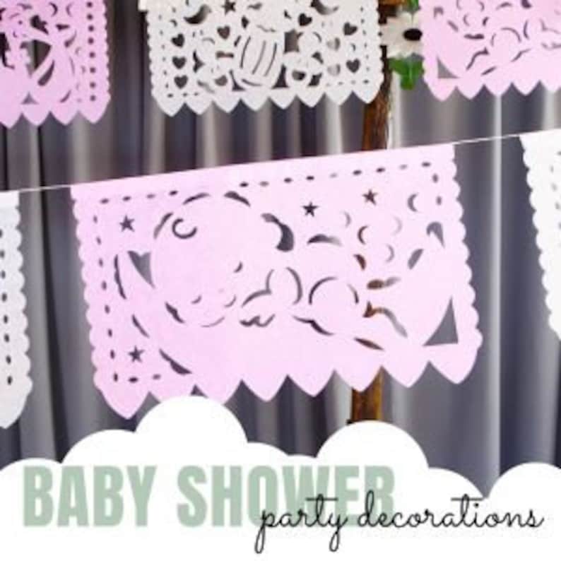 May include: Pink and white paper cutouts with a baby theme, including a baby, stars, and moons. The cutouts are strung together to form a banner that says "BABY SHOWER party decorations".
