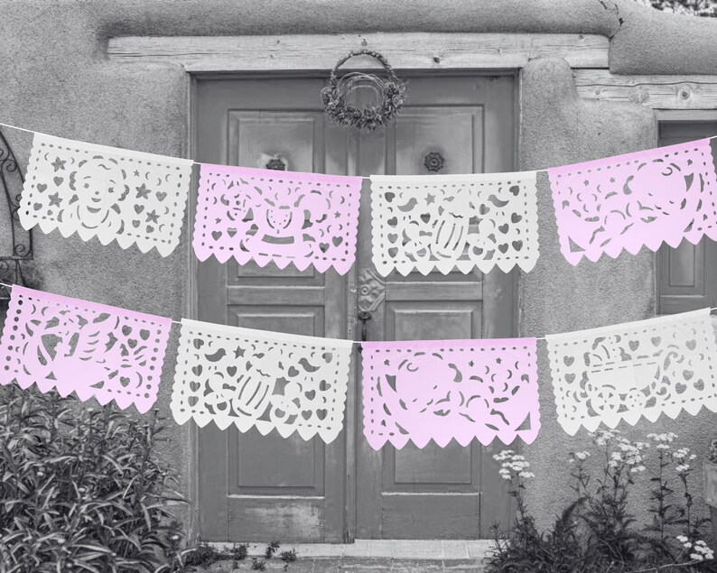 May include: A string of pink and white paper banners with cut-out designs, hanging in front of a doorway. The banners feature various designs, including hearts, stars, and other festive motifs.