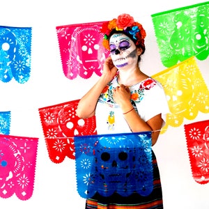 May include: A woman wearing traditional Day of the Dead makeup with colorful paper decorations in the background. The decorations feature a skull design and are strung together in a festive garland.