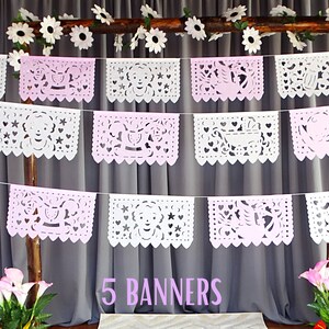 May include: Five white paper banners with pink accents and cut-out designs hang from a wooden branch. The banners feature various baby-themed designs, including a carriage, a star, and a heart. The text "5 BANNERS" is printed below the banners.