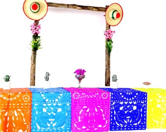 May include: A table setting with five colorful paper table runners with intricate cut-out designs. The table runners are orange, blue, pink, blue, and yellow. The table is decorated with small potted cacti and flowers.
