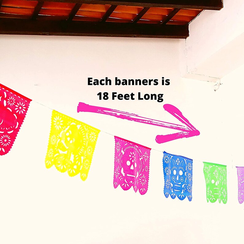 May include: A string of colorful paper banners with a skull design hangs on a white wall. The text "Each banners is 18 Feet Long" is written on the wall with a pink arrow pointing to the banners.