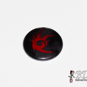 Op de afbeelding: Een zwarte knop met een rood en zwart gestileerd logo van een halve maan met punten. Het logo lijkt op het logo van het videogamepersonage Shadow the Hedgehog.