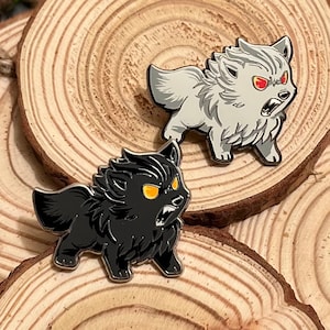 May include: Two enamel pins of cartoon wolves. One wolf is white with red eyes and the other is black with yellow eyes. Both wolves have a snarling expression.