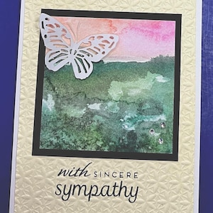 Könnte beinhalten: Beileidskarte mit einer Aquarelllandschaft in Grün, Rosa und Orange. Ein weißer Schmetterling ist oben links angebracht. Die Karte hat einen strukturierten, cremefarbenen Hintergrund mit dem Text "with sincere sympathy".