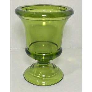 May include: A green glass vase with a pedestal base. The vase has a wide, flared rim and a bulbous midsection. The glass is a translucent green color. The vase is likely used for decorative purposes or to hold flowers.