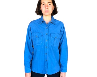 May include: A long-sleeved, blue button-down shirt with two flap pockets on the chest. The shirt has a classic collar and a button-up front.