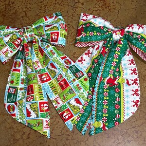 May include: Two decorative fabric bows featuring Grinch-themed patterns. The left bow displays a grid of colorful squares with Grinch illustrations and text. The right bow features vertical stripes of green, white, and red with peppermint and Grinch motifs.