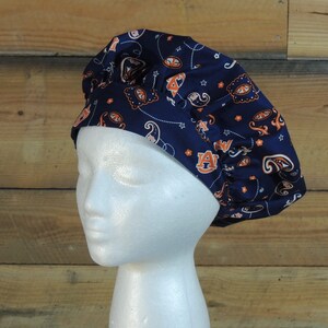 May include: A blue scrub hat with a paisley pattern and orange and white accents. The hat has the letter "A" in orange on the front.