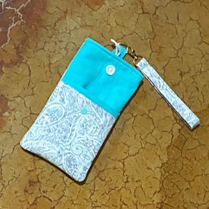 May include: A turquoise and white paisley patterned phone pouch with a snap closure and a matching strap.