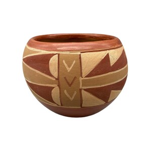 May include: A round, hand-painted ceramic bowl with a wide opening. The bowl features a reddish-brown exterior and rim, with tan and reddish-brown geometric patterns. The design includes triangles, chevrons, and curved lines.