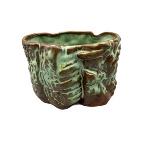 May include: A small, ceramic planter with a textured, rock-like exterior. The planter features a blend of brown and green glaze, with the interior a solid green. The irregular shape adds to its unique, natural aesthetic.