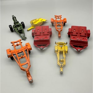 May include: A collection of vintage toy trailers in various colors, including red, orange, yellow, and green. The trailers have different designs and sizes, with visible details like wheels and hitches. Some show signs of wear, suggesting they are well-loved toys.