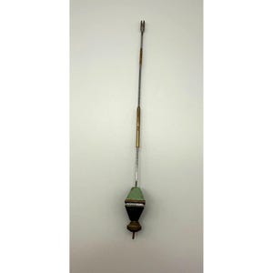 May include: A vintage metal pendulum with a long, slender rod. The pendulum features a green and black geometric weight, brass accents, and a small, pointed tip. The top has a fork-like design.