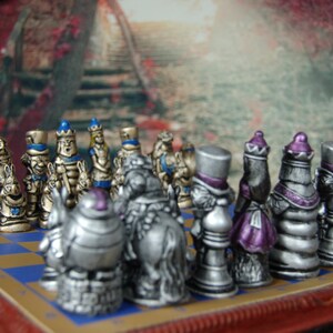May include: A silver and blue chess set with various characters from Alice in Wonderland. The pieces are arranged on a wooden chessboard with a red border.