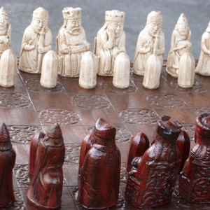 May include: A wooden chessboard with white and red chess pieces. The white pieces are made of a light-coloured wood and are in the shape of bishops, rooks, knights, and pawns. The red pieces are made of a darker wood and are in the shape of bishops, rooks, knights, and pawns.