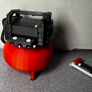 May include: A red air compressor with a black top and a white air hose. The compressor is sitting on a gray surface. There is a white and red air gun next to the compressor.