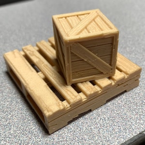 May include: A small wooden crate sits on a wooden pallet. The crate is made of light brown wood and has a diagonal brace across the front. The pallet is made of the same wood and has a simple design.