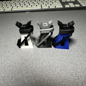 May include: Three small, 3D printed car jacks in white, gray, and blue. The jacks are designed to lift a car or other heavy object.