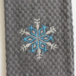 May include: A gray kitchen towel with a blue and white embroidered snowflake design.