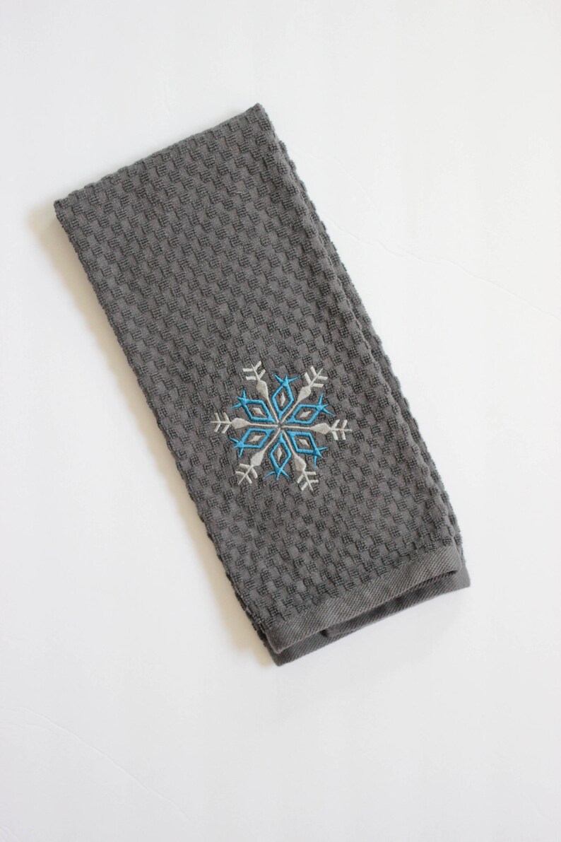 May include: A gray waffle weave kitchen towel with a blue and white embroidered snowflake design.
