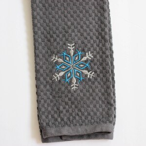 May include: Gray kitchen towel with a blue and white embroidered snowflake design.
