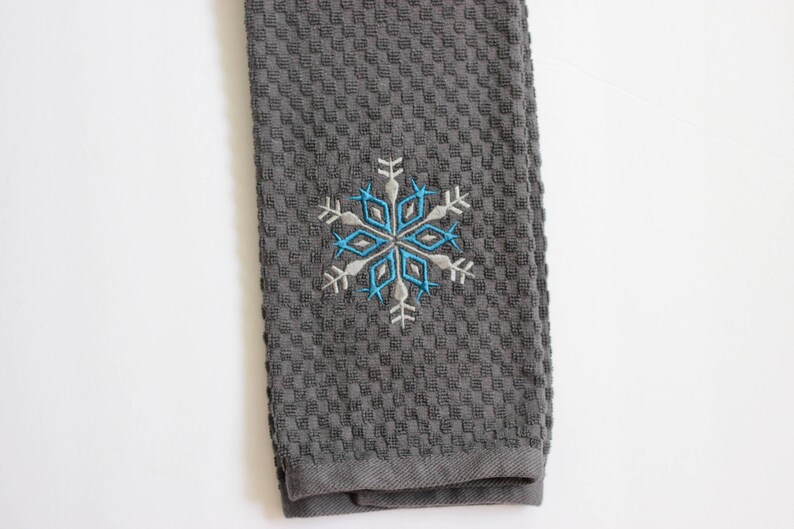 May include: Gray kitchen towel with a blue and white embroidered snowflake design.