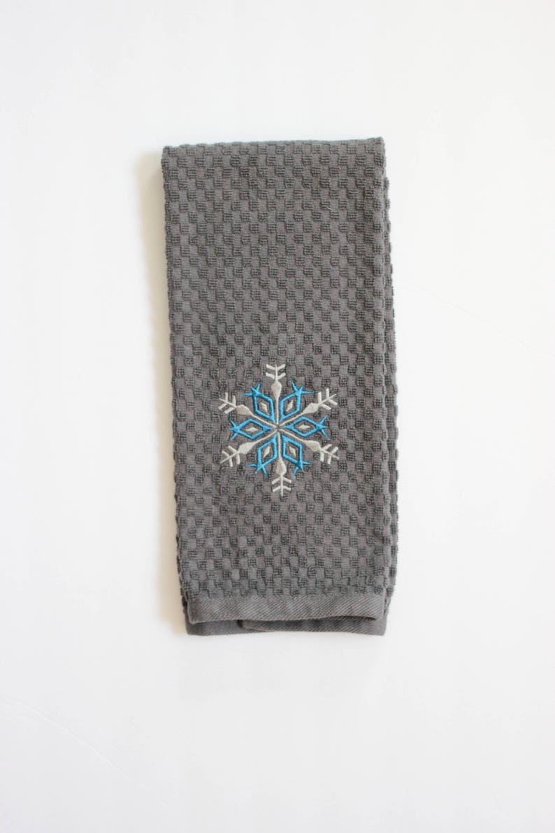 May include: A gray kitchen towel with a blue and white snowflake embroidered on it.