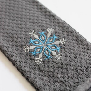 May include: A gray waffle weave kitchen towel with a blue and white embroidered snowflake design.