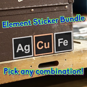 Puede incluir: Un paquete de pegatinas Element Sticker Bundle con tres pegatinas cuadradas con los símbolos químicos Ag, Cu y Fe. Las pegatinas tienen fondos negros con letras blancas o de color cobre. El texto Element Sticker Bundle y Pick any combination! es visible.