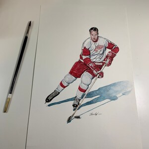 May include: A watercolor painting of a hockey player wearing a red and white jersey with a winged wheel logo. The player is skating with a hockey stick and puck. The painting is signed "Stanley 20".