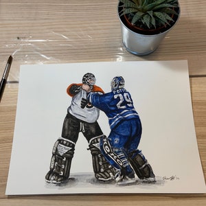 May include: A watercolor painting of two hockey players in action. The player on the left is wearing a black and orange uniform with a white helmet and is in a goalie stance. The player on the right is wearing a blue and white uniform with a white helmet and is skating towards the goalie. The text "POITRAS 29" is on the back of the player's jersey.