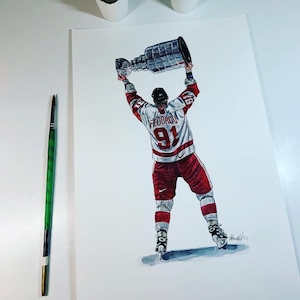 May include: A hand-drawn illustration of a hockey player in a red and white jersey holding a silver trophy above their head. The player is wearing a white helmet and has the number 91 on their jersey. The jersey has the name "FEDOROV" on the front. The player is standing on a white background.