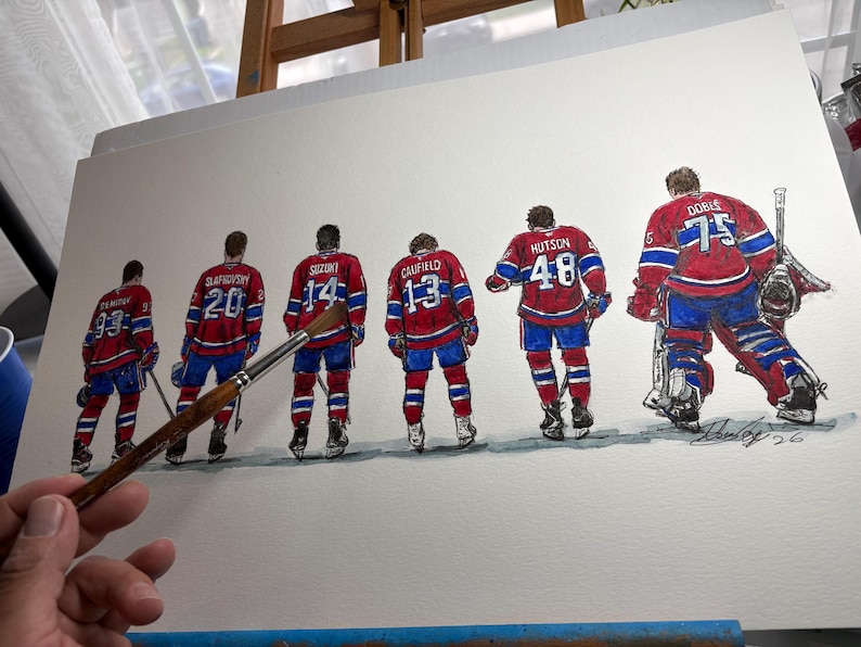 Puede incluir: Pintura a la acuarela de seis jugadores de hockey sobre hielo con uniformes rojos, blancos y azules, vistos por la espalda. Cada camiseta muestra un n&uacute;mero diferente. Un pincel se sostiene frente a la obra de arte. La pintura est&aacute; sobre un lienzo blanco.
