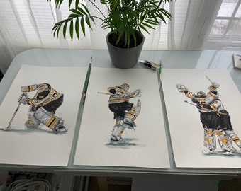 May include: Three black and white watercolor paintings of hockey players in goalie gear. The players are wearing a yellow and black jersey with the word "Bruins" on the front. The paintings are on white paper and are framed in black.