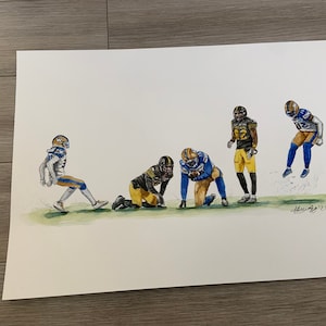以下が含まれることがあります： 5人のアメリカンフットボール選手がアクションを起こしている水彩画。選手は青と金のユニフォームを着て、黒いヘルメットをかぶっています。絵は白い背景に描かれており、右下に署名があります。
