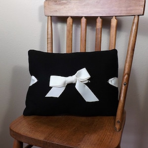 May include: A black pillow with a white satin bow on a wooden chair.