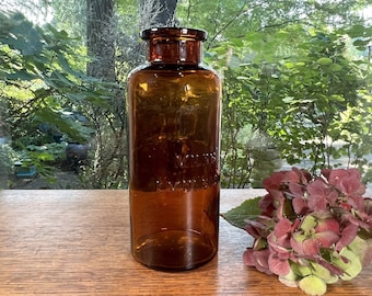 May include: A dark amber glass bottle with a wide mouth and a glass stopper. The bottle has embossed lettering that reads "Vicks VapoRub".