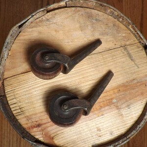May include: Two antique wooden wheels with metal axles. The wheels are brown and have a worn finish. The axles are black and have a simple design.