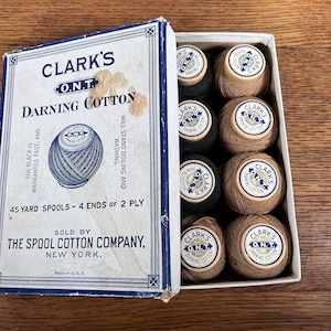 May include: A box of Clark's O.N.T. Darning Cotton spools. The box is blue and white with the text "Clark's O.N.T. Darning Cotton" and "45 yard spools - 4 ends of 2 ply". The box contains 8 spools of cotton thread, 4 black and 4 brown.