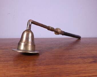 May include: A brass candle snuffer with a long, black handle. The snuffer has a bell-shaped top and a wide base.
