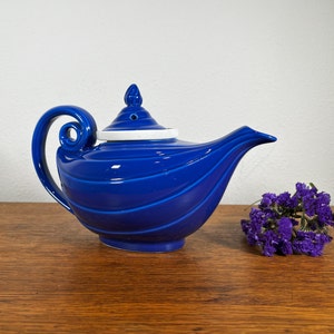 May include: A blue ceramic teapot with a white lid and a swirling design. The teapot is shaped like a genie lamp.